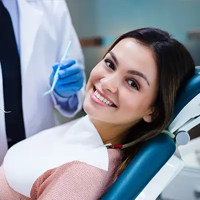  An woman smiling in a dentist chair while dentist waits with his tools.