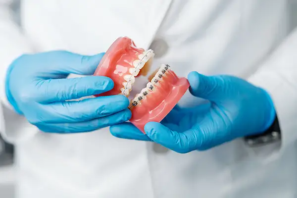 A dentist's gloved hand holding a dental model with metal braces to explain orthodontic treatment options.